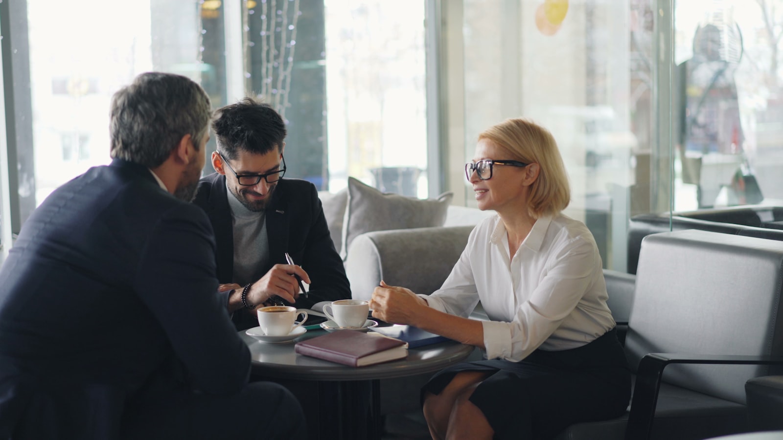 Three colleagues in conversation around a table with documents.