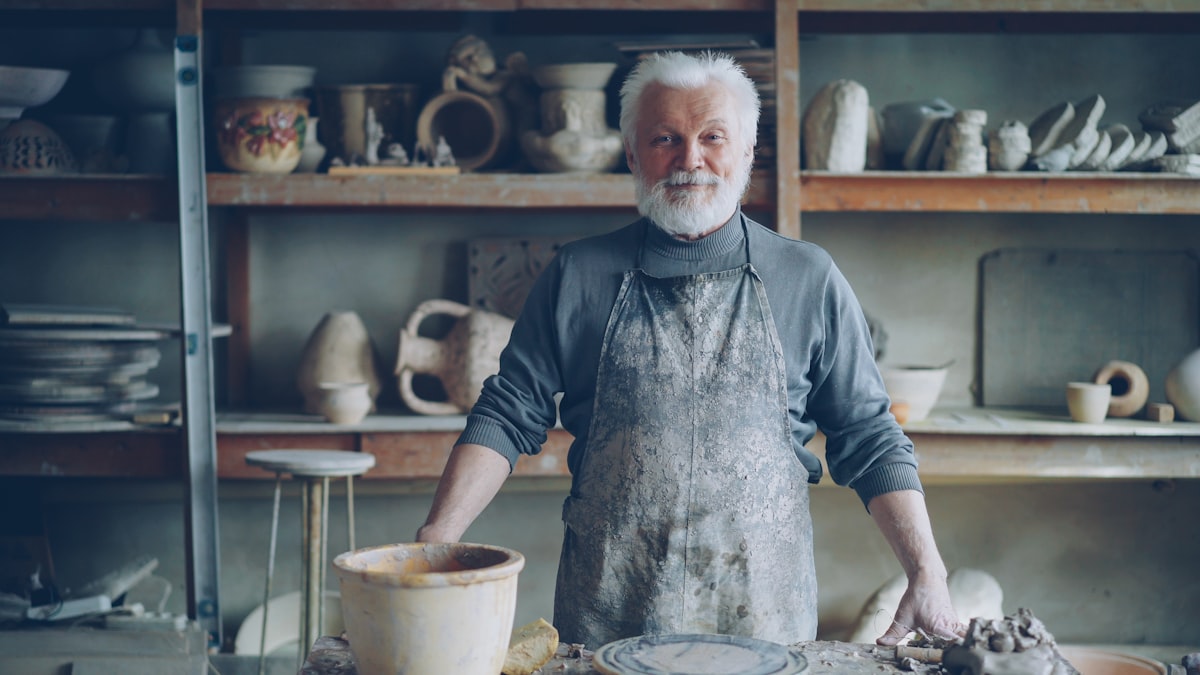A potter standing in his studio beside finished work.